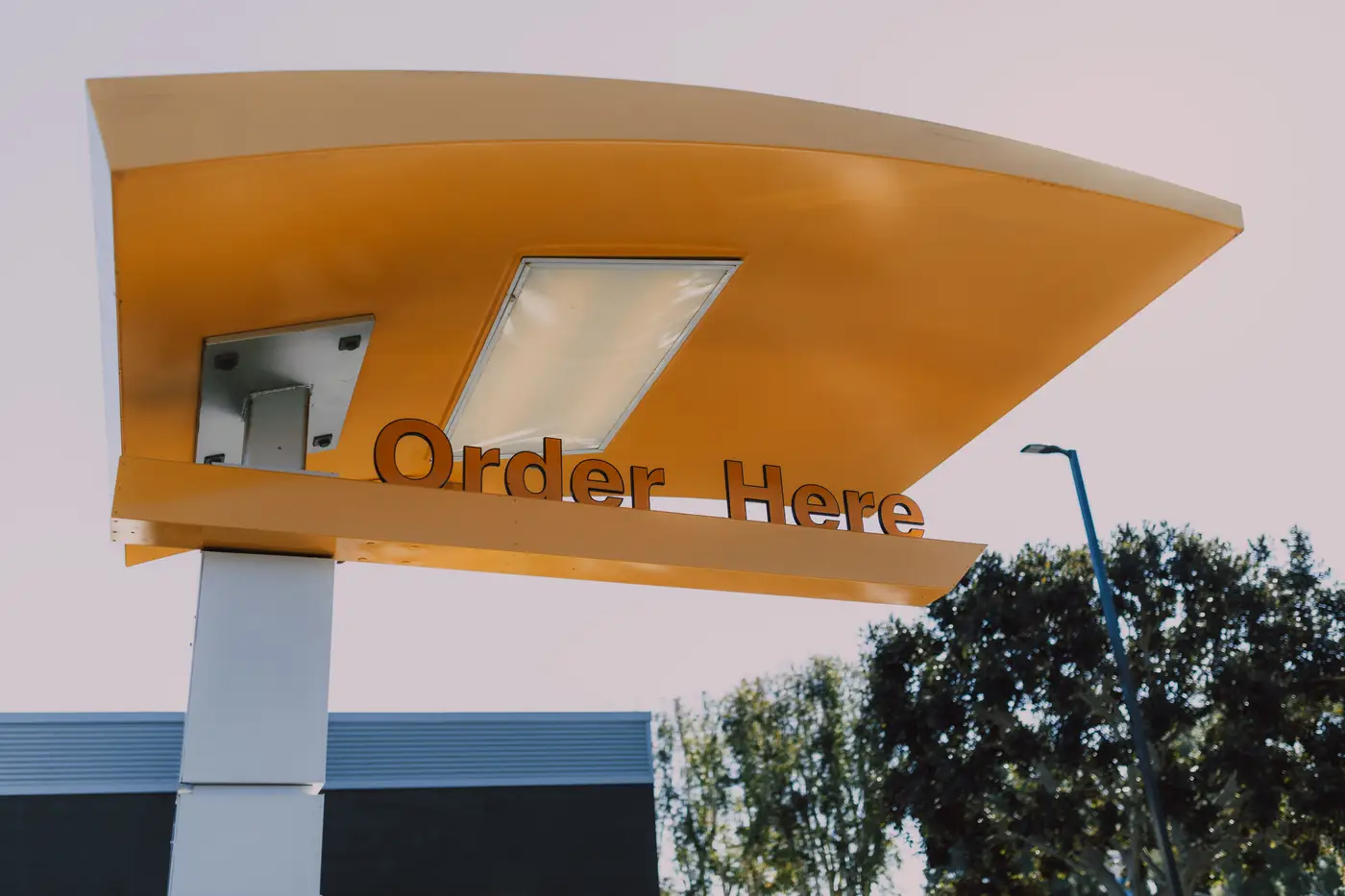 A drive-thru order canopy with a blank 'Order Here' sign, photographed in daylight, no branding visible.